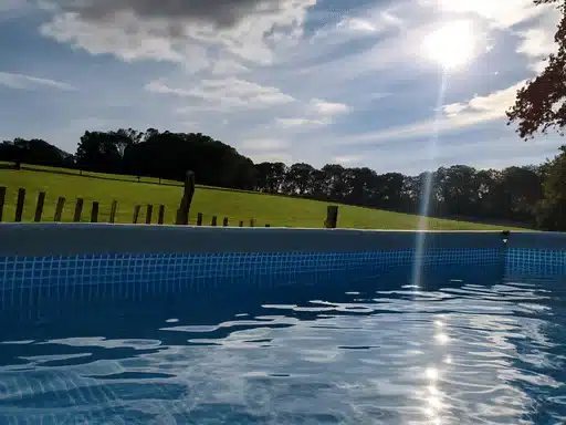 L'eau de la piscine des Cabanes Champêtres au premier plan, face à la prairie clôturée et aux arbres